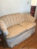 Front view of the beige loveseat with floral patterned upholstery, two cushioned seats, skirted base and curved scalloped back.