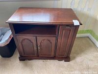 Frontal image showing the wooden nightstand with one open shelf and three cabinet doors, detailing the handles and surface condition.
