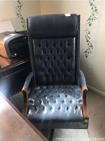 Front view of black tufted leather office chair with wood armrests and brass nailhead trim showing overall condition.