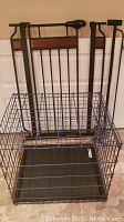 Front angle of black metal wire pet crate with black tray bottom, showing crate folded or partially disassembled with black metal gate frame behind