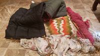Two Coleman sleeping bags, chevron patterned afghan, pink knit hammock, and window treatment with hanging rod and hardware laid out on tile floor.