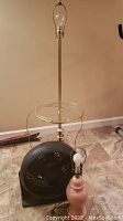 Full view of floor lamp with brass pole, circular glass table and black base fan underneath.