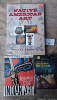 Photo showing all three books: 'Native American Art' by William C. Ketchum, Jr., 'Seattle World's Fair 1962 Northwest Coast Indian Art', and 'Sing Down the Moon' by Scott O'Dell