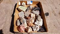 Wide view of all assorted rocks and minerals in a cardboard box showing various sizes and colors.