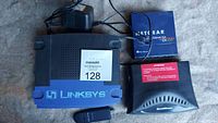 Photo showing Linksys DSL modem/router, Speedstream DSL modem/router, Netgear EN 104TP ethernet hub with its box, and Belkin USB WiFi adapter.