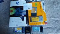 Five PC cards and accessories displayed including the boxed Netgear WiFi Card and Apricorn adapter with additional cards laid out.