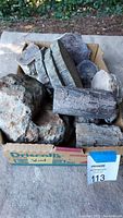 Box filled with thick slabs and chunks of petrified wood showing rough and cut surfaces with natural green and brown hues.