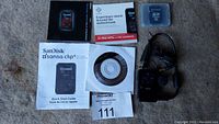 Photo showing SanDisk Sansa Clip MP3 player, charging cord, Quick Start Guide, factory manuals, MaxSold lot card, and installation CD.
