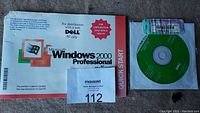 Microsoft Windows 2000 Professional installation CD with Dell branding, manual, and Quick Start guide shown together on a surface.