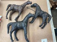 Photo showing three antique horse figurines lying on a flat surface, visible saddles and wear details