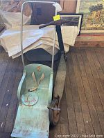 Photo of antique child's sled showing light green wooden painted seat with Sno-Ette logo, metal frame, upright handle bars with grips, and seat belts.