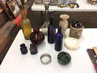 Overview of lot featuring glass bottles, pottery vases, stone dish, and jug with text.