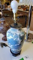 Front side view of the ceramic lamp showing blue and white floral design with a light bulb and brass socket fitting.