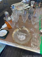 Full view of cocktail shaker, etched crystal bowls, glassware, and scenic coasters on table.