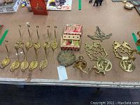 Full lot view showing ten brass wall hooks, two brass candle sconces, brass dish or leveler, and boxes of Paris candles on tabletop.