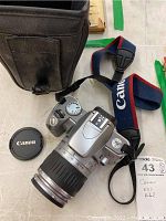 Photo showing Canon EOS Rebel Ti camera with 28-90mm lens attached, Canon lens cap, Canon strap, and Vanguard case laid out on a flat surface.