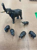 Six elephant figurines: four wooden varying sizes, two cast iron, all displayed on a carpeted floor.