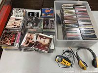 Stacks of assorted music CDs laid out on a table with a plastic bin full of CDs and a yellow and black Sony Walkman with wireless headphones.