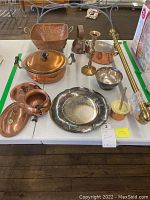 Photo showing multiple copper and brass kitchenware items including bowls, lidded pots, a candlestick, and a curtain rod.