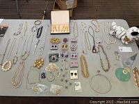 Full overhead view of the costume jewelry collection including necklaces, bracelets, brooches, earrings, perfume bottles, and a plush toy on a table.