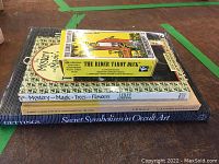 Stack of three books with Rider Tarot Deck box on top, titles visible: 'The Mystery and Magic of Trees and Flowers', 'Tarot cards for fun and fortune telling', and 'Secret Symbolism in Occult Art'.
