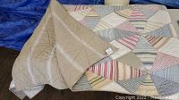 Quilt folded showing reverse solid light brown side and patchwork colored side on floor with wood planks