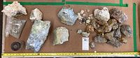 Wide assortment of rocks and minerals arranged on cardboard, showing size scale with ruler and green tape