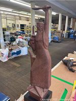 Full side view of the tall metal sculpture showing texture, robe, beard, sword, and scroll with warehouse background