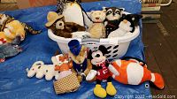 Photo showing assortment of stuffed animals and handcrafted plush in a basket and around it on a blue tarp.
