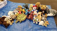 Overview of the lot on blue tarp showing all stuffed animals together with Steiff Orsi bear and the green turtle plush prominent