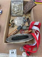 Full view of lot items in cardboard box including swim medals, Trojan plaque, bottle openers, letterbox sign, lock, and straight razor.