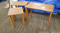 Three wooden nesting tables arranged standing separately on a wooden floor with visible wood grain and scratches.