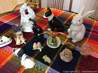 All figurines arranged on colorful plaid cloth showing various rabbits, birds, cat, and flower vase figurine