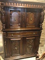 Front view of antique wooden armoire showing carved doors, turned pillar style sides, and brass hardware.