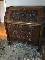Front view of carved oak secretary desk showing drop-front panel and three lower drawers