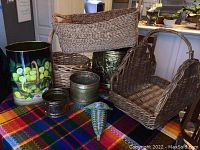 Photo showing multiple woven baskets of various shapes and sizes grouped together with a large decorative brass container and small metal containers on a colorful tablecloth.
