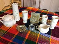 Overall grouping on multicolor tablecloth showing Belleek porcelain vase, teapot, mugs, creamer, plus ashtray, plaque and small bud vase