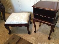 Wooden stool and mahogany side table with drawer and open shelf on tiled floor