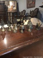 Seven brass bells displayed on wooden table, showing variety in design and size