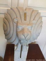 Front and side views of lion head bust sculpture showing full textured mane, facial details, and metal rod through center.