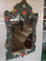 Front view of the full decorative mirror showing carved floral and leaf motifs on the frame with multicolor paint.