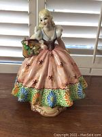 Front view of the colorful Italian porcelain figurine of a woman holding a basket of flowers, showing detailed floral painting on dress and basket contents.
