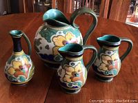 Four Gouda Royal Pottery ceramic pieces with floral and scroll patterns on a wooden table, illustrating full set and design details.