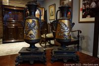 Pair of tall ornate metal incense urns with gold-tone bodies and dark metal bird reliefs on decorative plinth bases.