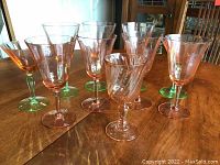 Photo of nine pink glass stemware pieces arranged on a wooden table showing different shapes and bases.