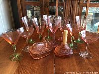 Photo of set of pink stemmed glassware with green stems, pink glass covered rabbit dish and pink glass candle holder on wooden table
