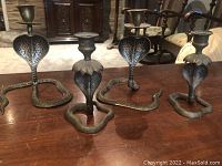Group of four brass snake candle holders on wood surface in living room