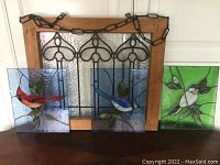Four stained glass panels displayed together: one framed clear panel and three bird panels