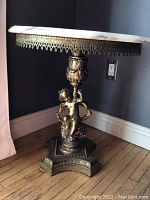 Full view of round marble top table with bronze ornate cherub figure base, showing the marble chip.