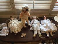 Four vintage porcelain dolls displayed side by side on a surface near a window. Dolls have vintage style clothing and accessories. One doll wears an eye patch.